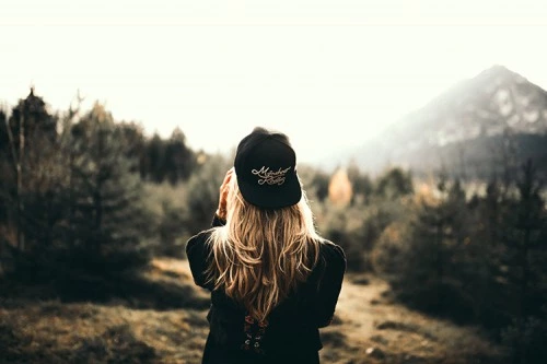 a girl near the trees looking at the mountains